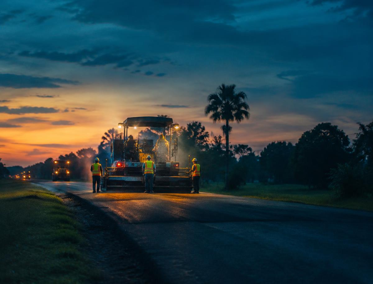 An asphalt paving crew and machinery at dusk, seen from a distance